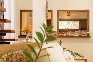 Zona de recepción de hotel con una pared de piedra, un jarrón con flores y un mostrador de buffet con alimentos etiquetados.
