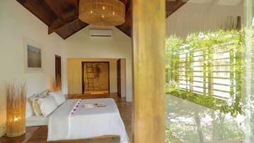 Une chambre avec un lit, un plafond en bois, un luminaire suspendu et une vue sur la verdure à l’extérieur.