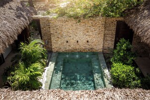 Una piscina infinita de piedra con agua cristalina, rodeada de exuberante vegetación y estructuras con techo de paja.