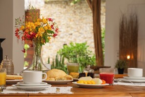 A breakfast setting with a variety of dishes, a vase of flowers, and a view of a stone wall. - Villa Alegria - La Villa Group (Jijoca de Jericoacoara)