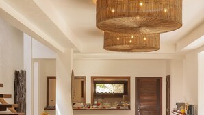 A modern living room with a large woven ceiling light fixture, a stone accent wall, and a wooden bench. - Villa Alegria - La Villa Group (Jijoca de Jericoacoara)