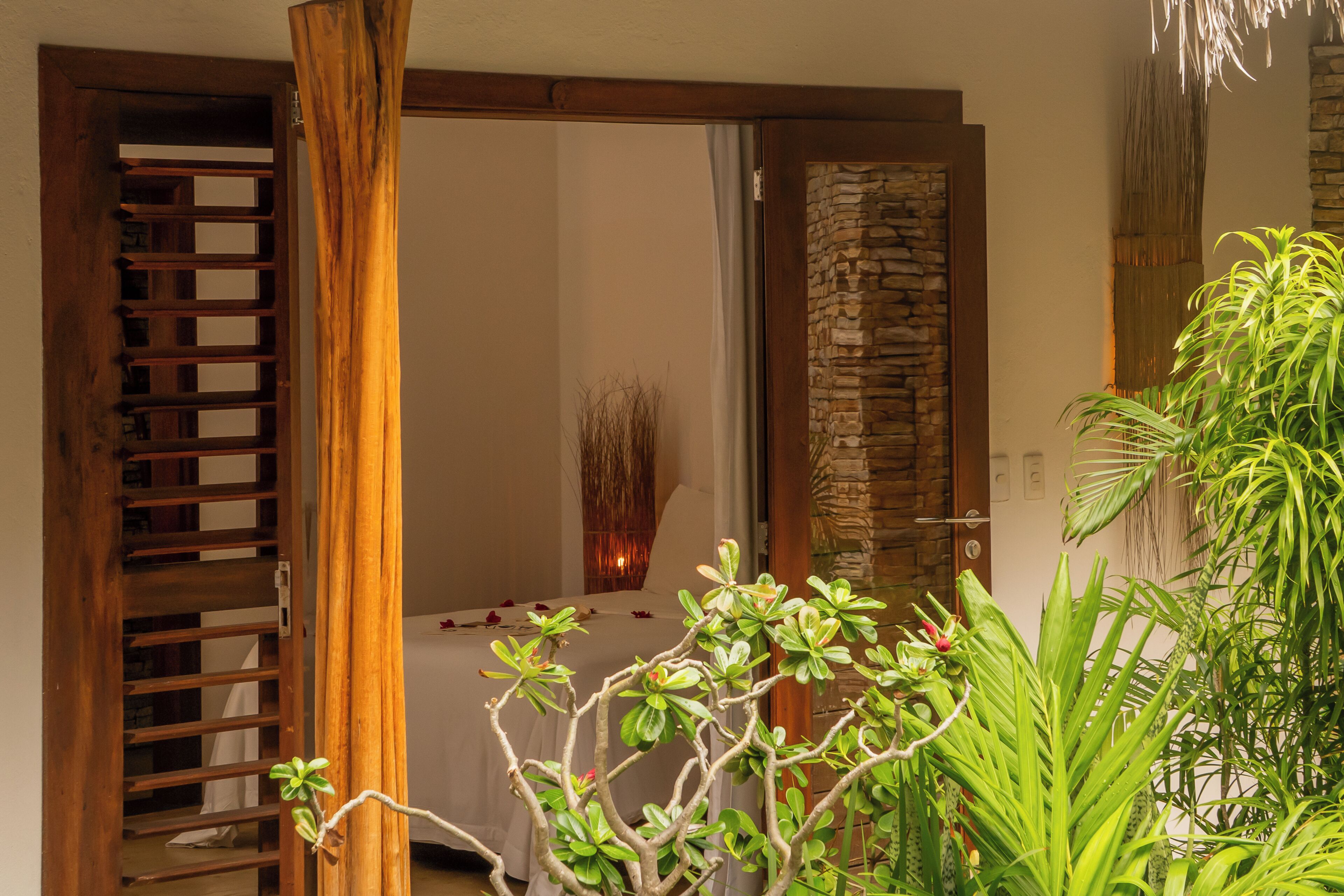 Una habitación con puerta de madera, pared de piedra y una cama con cubrecama blanco.
