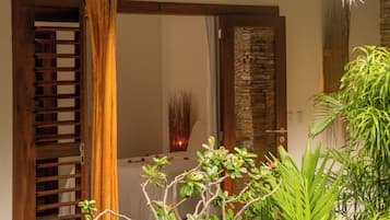 Una habitación con puerta de madera, pared de piedra y una cama con cubrecama blanco.