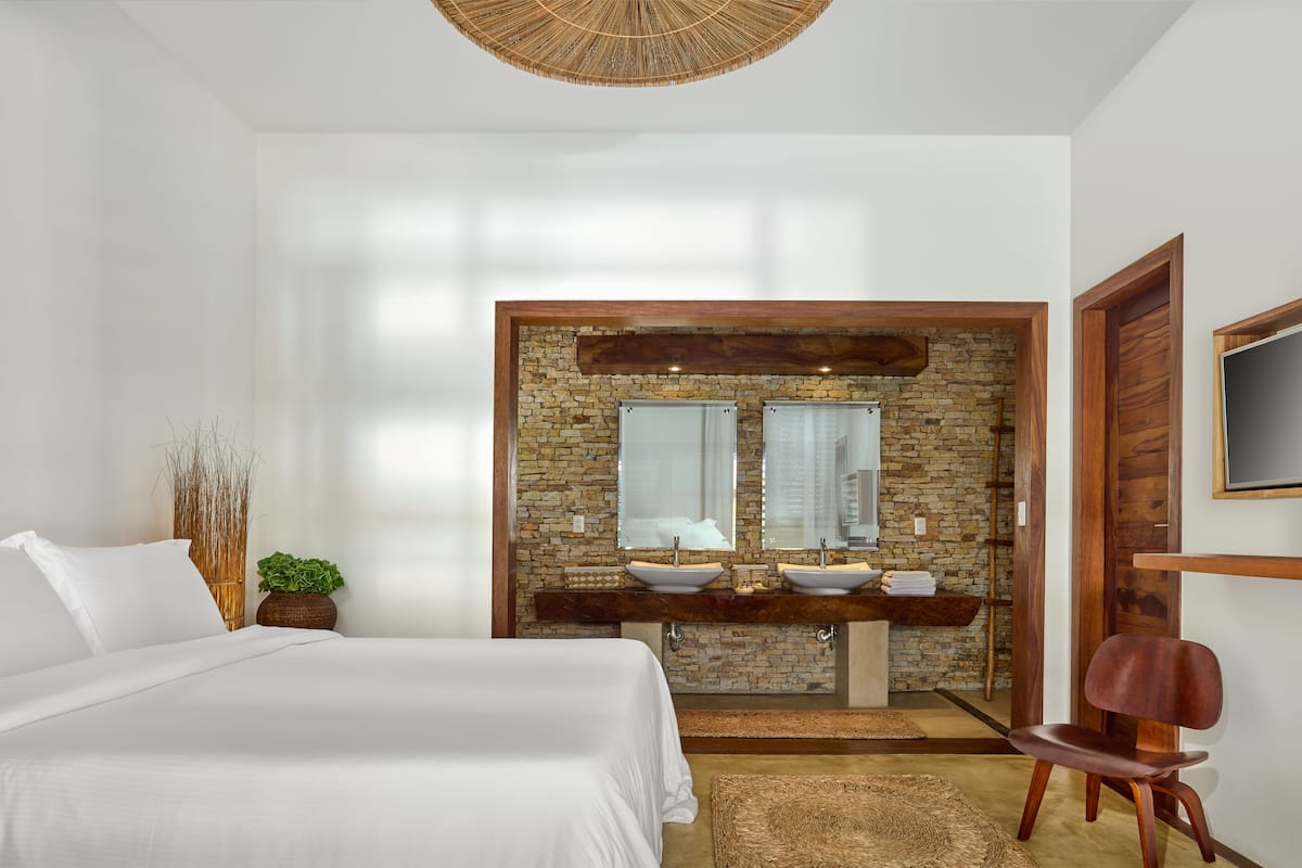 A bedroom with a large bed, a wooden vanity with a stone backsplash, and a mirror above the sink.