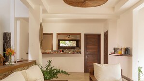 A modern living room with a sofa, a coffee table, and a dining area with a counter and chairs. - Villa Alegria - La Villa Group (Jijoca de Jericoacoara)
