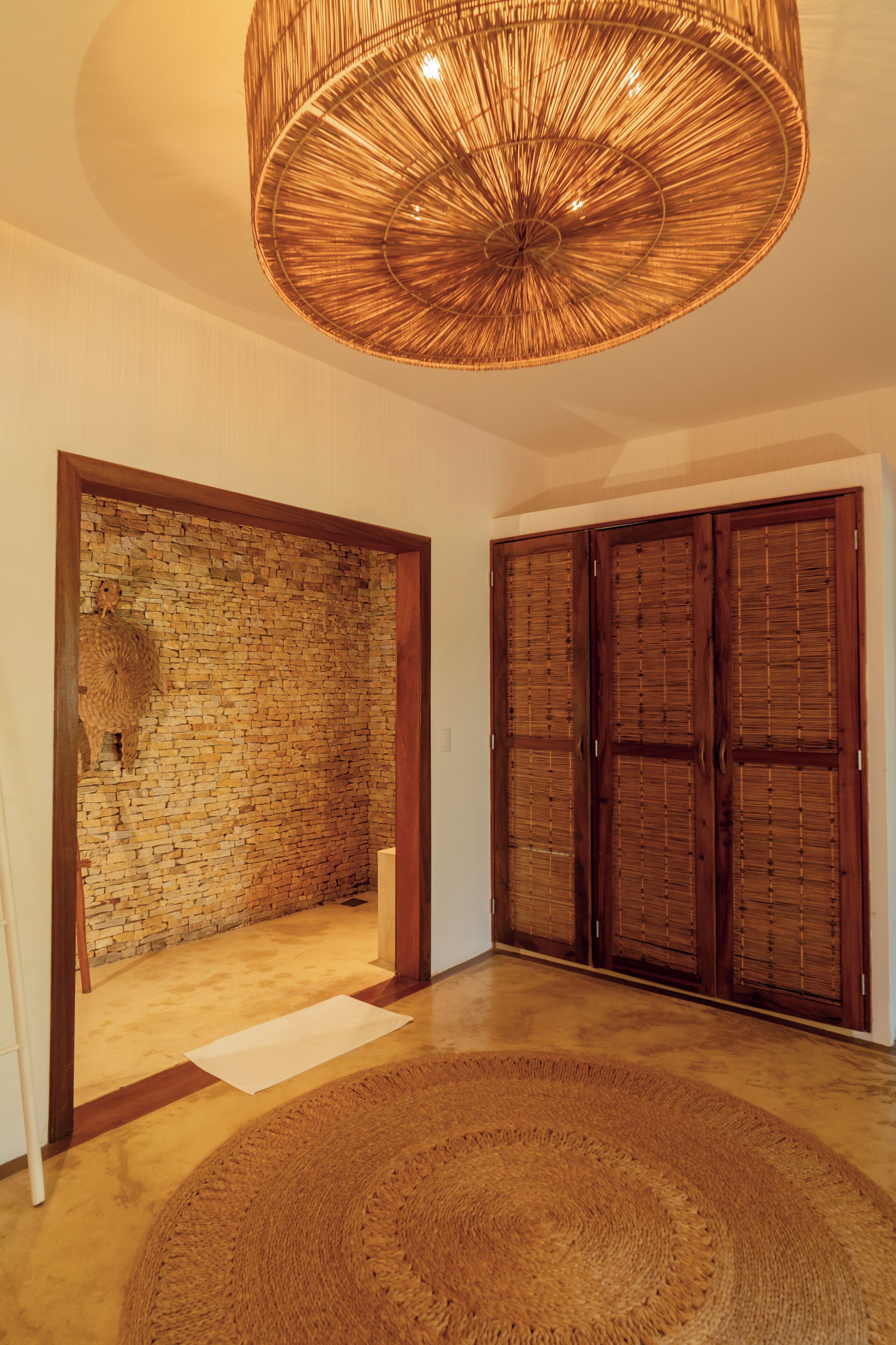 Una habitación con una lámpara de techo tejida, una pared de piedra y puertas de madera.