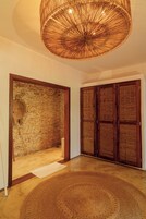 Una habitación con una lámpara de techo tejida, una pared de piedra y puertas de madera.