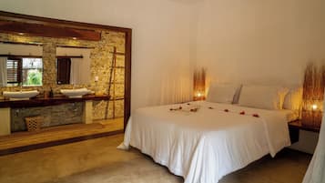 Une chambre avec un mur en pierre, une coiffeuse en bois, un lit avec du linge de maison blanc et un grand miroir.