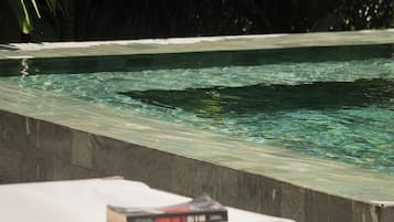 Un área de piscina con una silla de descanso y un libro, rodeada de follaje.
