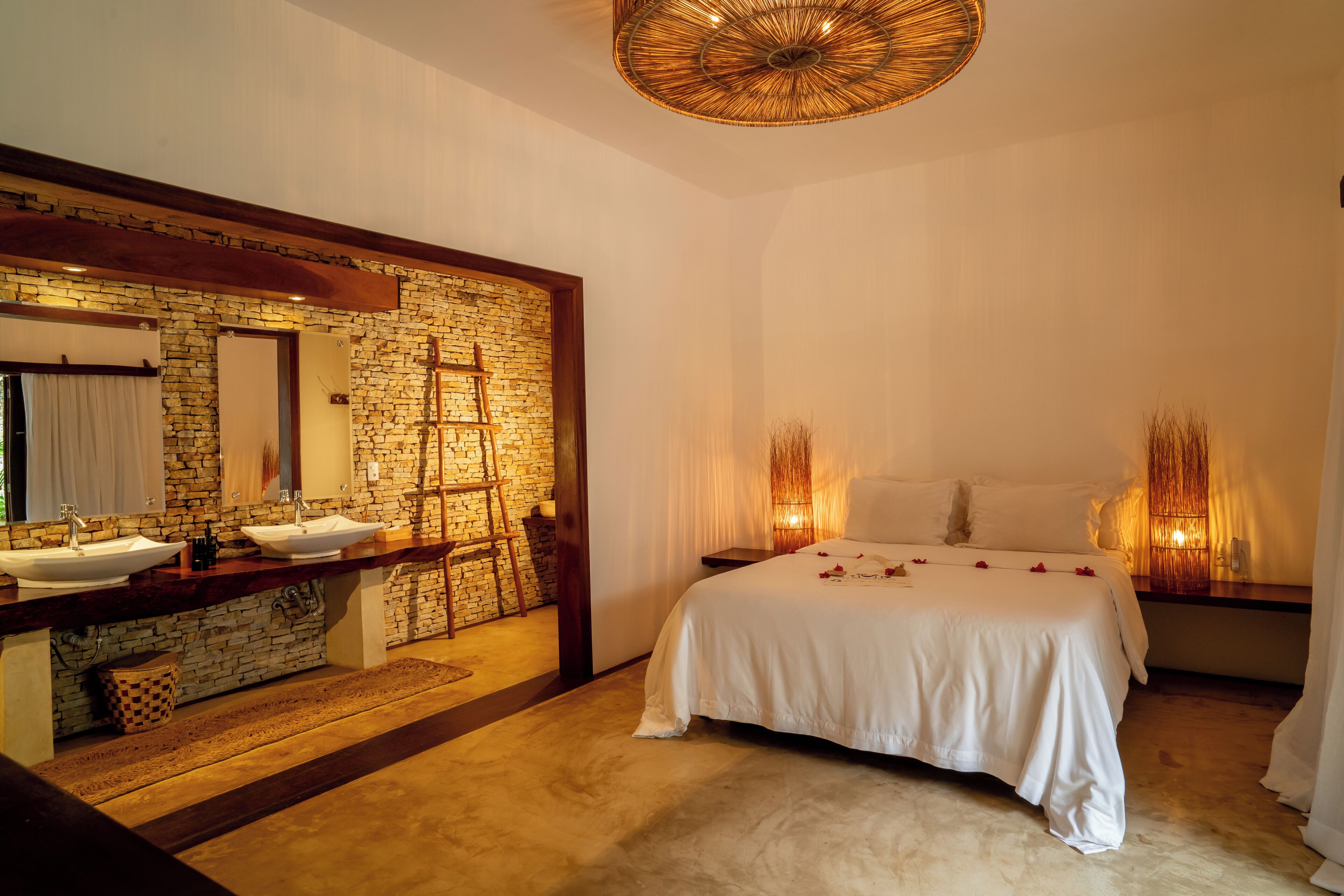 A bedroom with a stone wall, a large mirror, a bed with white bedding, and a wooden floor.