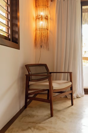 Una silla de madera con respaldo y asiento de mimbre, ubicada en una habitación con una lámpara fijada a la pared y un ventanal con cortinas.