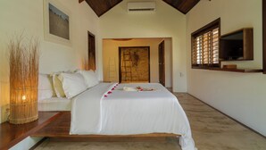 A bedroom with a bed, a wooden ceiling, a wall-mounted TV, and a door leading to another room. - Villa Alegria - La Villa Group (Jijoca de Jericoacoara)