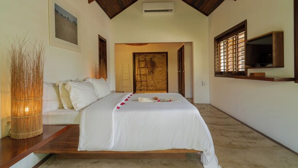 A bedroom with a bed, a wooden ceiling, a wall-mounted TV, and a door leading to another room. - Villa Alegria - La Villa Group (Jijoca de Jericoacoara)