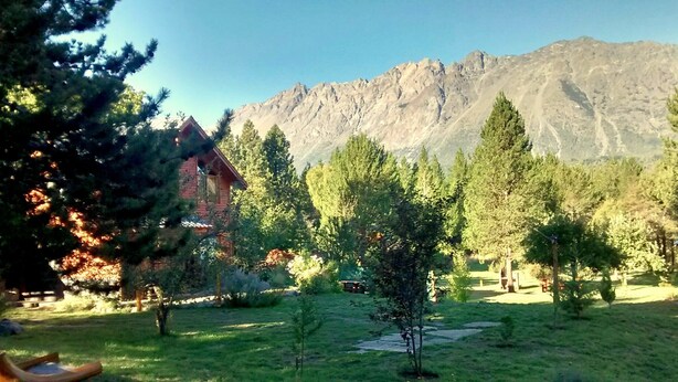 A rustic cabin surrounded by a forested area with a mountain backdrop. - Cabañas El Refugio de Puelo (Lago Puelo)