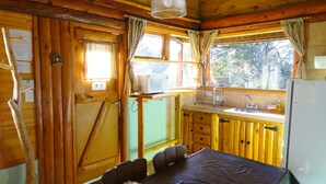 A wooden cabin interior with a dining table, chairs, a kitchenette with a microwave, sink, and refrigerator. - Cabañas El Refugio de Puelo (Lago Puelo)