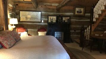 A log cabin bedroom with a large bed, a fireplace, wooden walls, and a staircase.