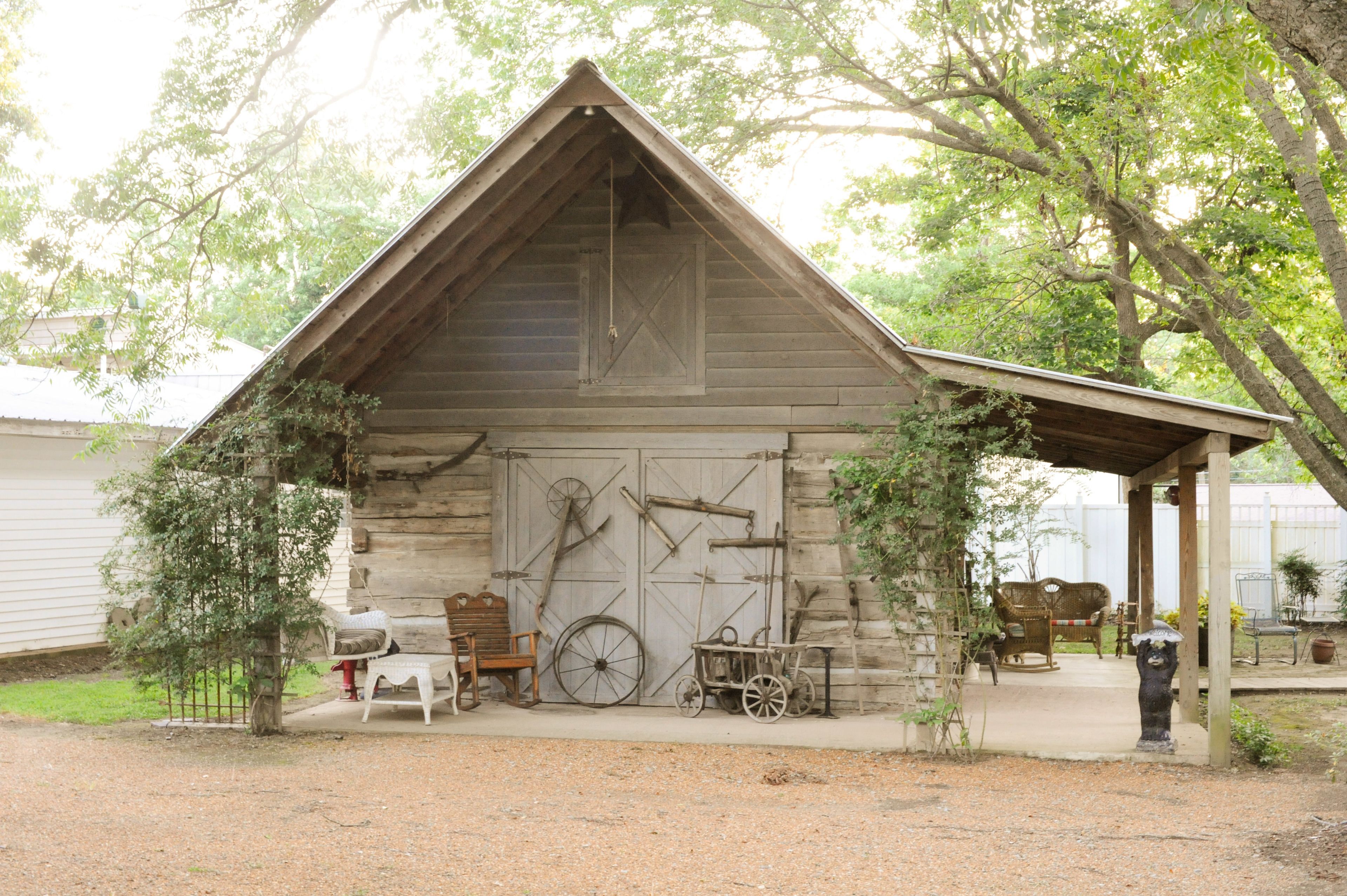 A rustic wooden cabin with a sloped roof, a porch, and a wheelbarrow.