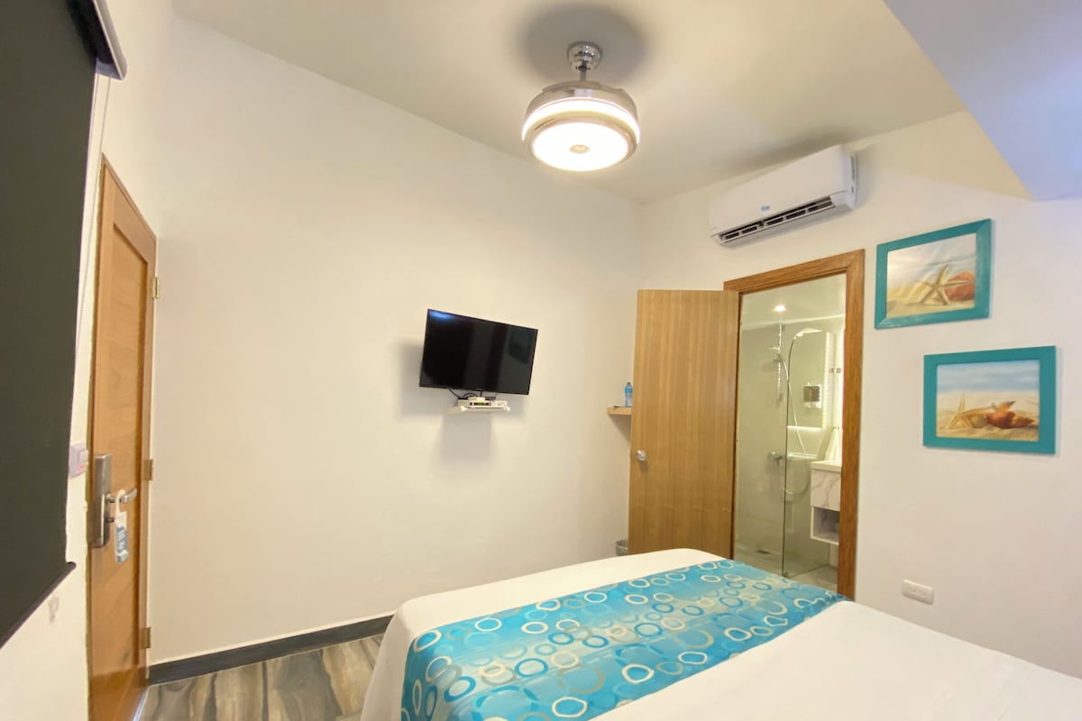 A bedroom with a bed, a television, a shower, and a door.