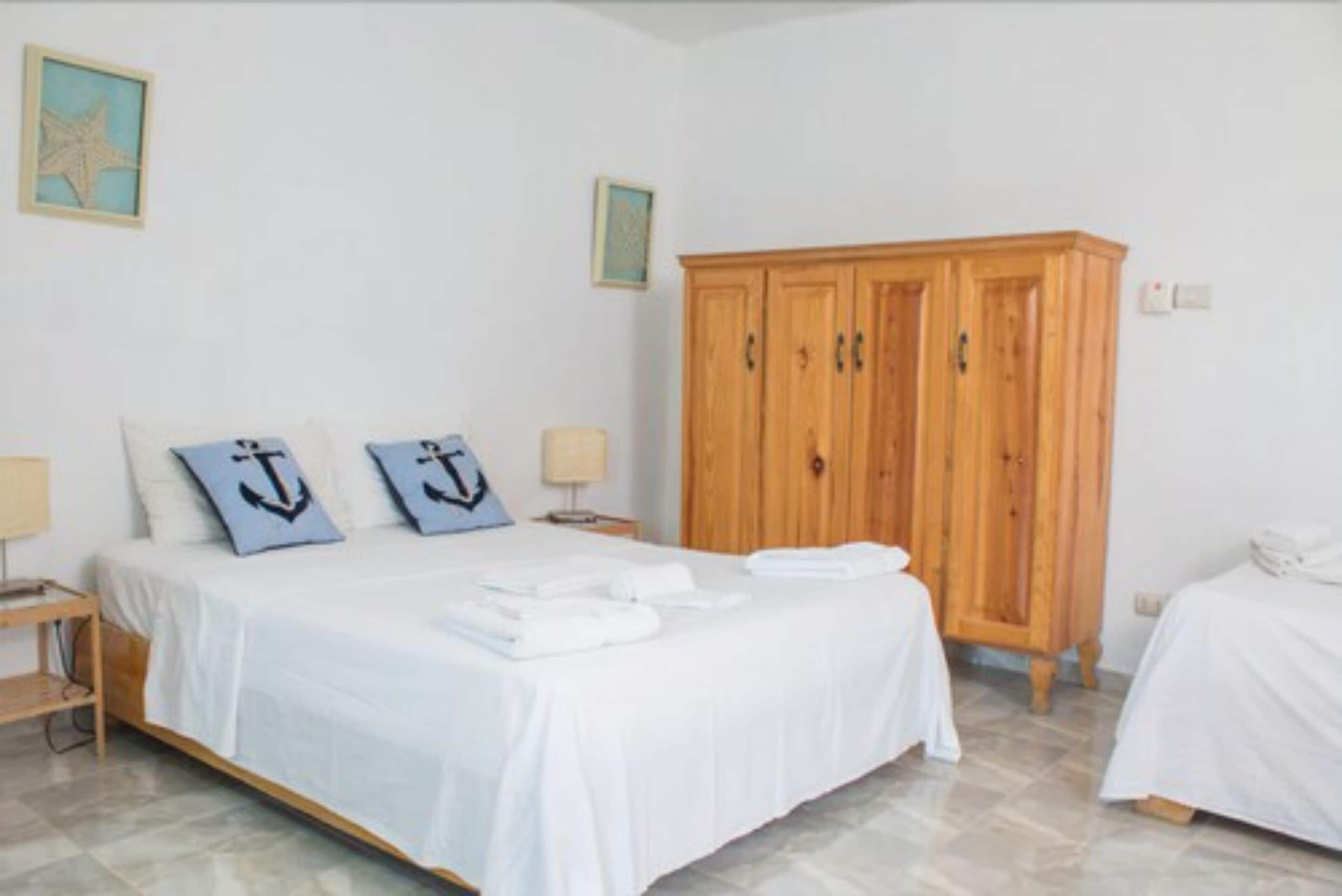 Un dormitorio con cama, dos mesitas de noche, un armario de madera y una pequeña mesa.