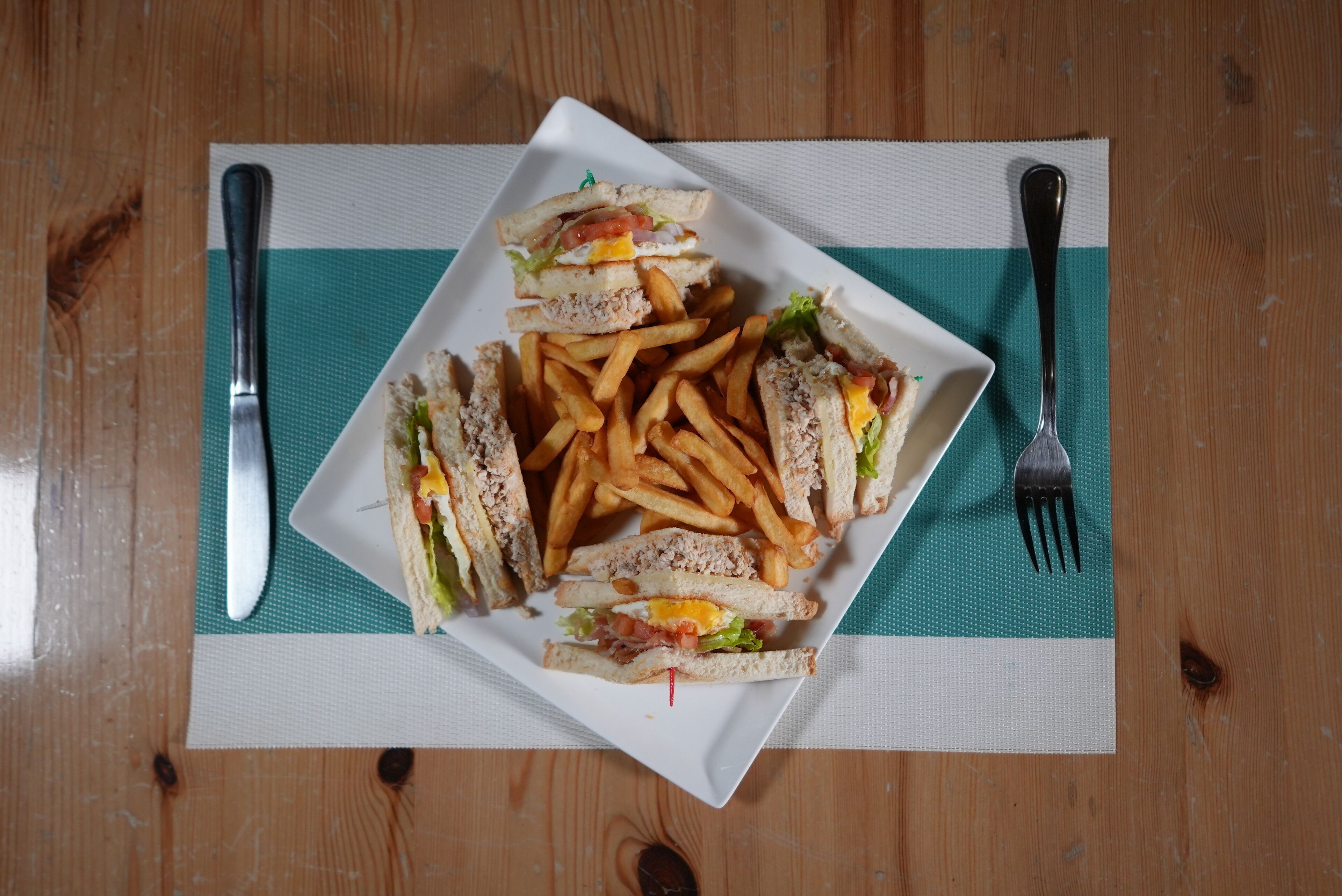 A plate of sandwiches and fries on a wooden table with a placemat.