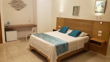 Un dormitorio con cama, escritorio, silla, refrigerador pequeño e iluminación de pared.