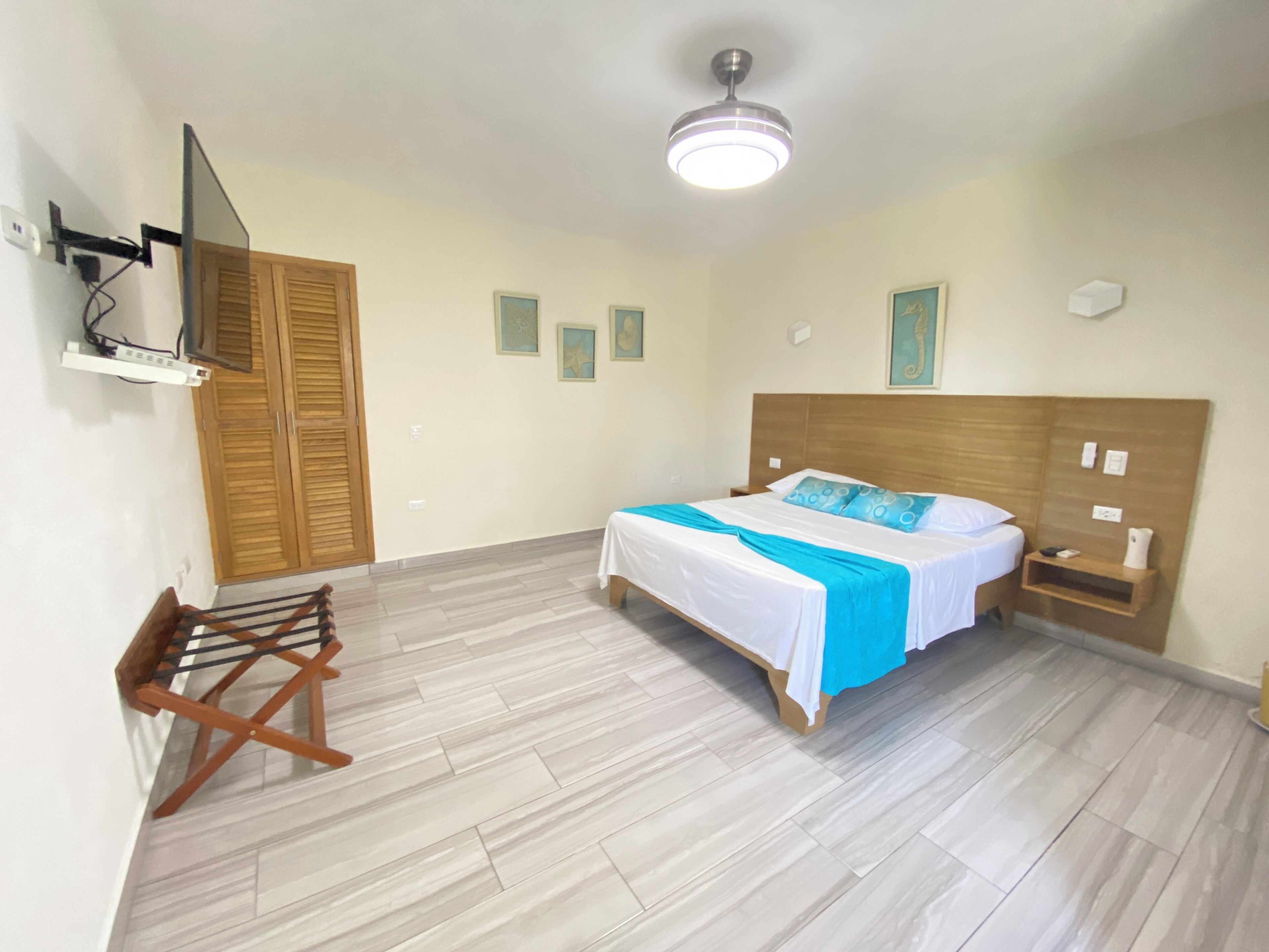 Een slaapkamer met een bed, een houten garderobe, een aan de muur bevestigde televisie en een plafondventilator.