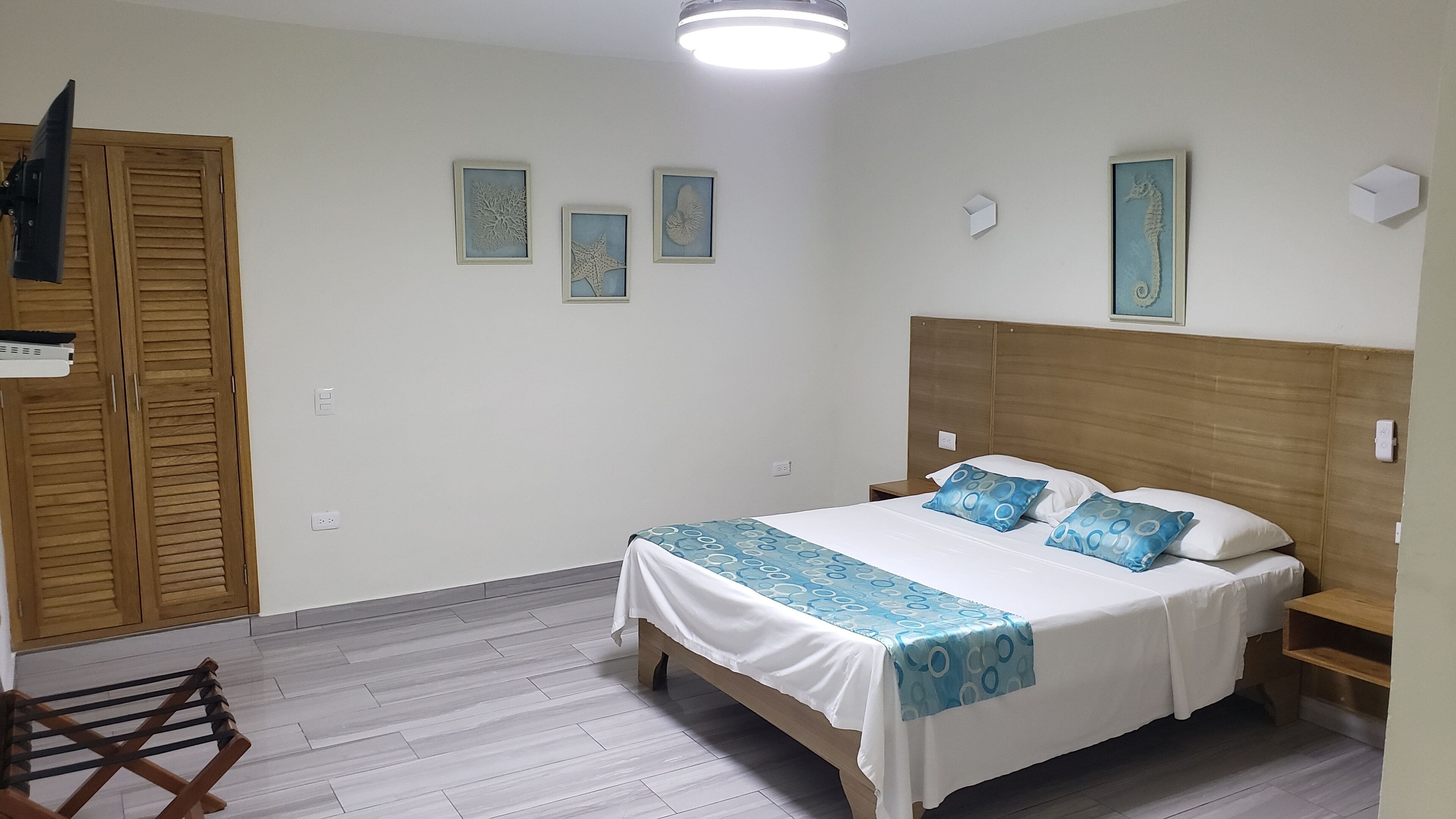 A neatly arranged bedroom with a bed, wooden wardrobe, and framed artwork on the wall.