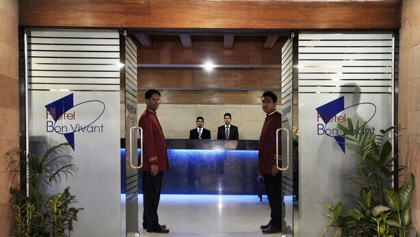 Modernilla designilla sisustettu hotellin vastaanottoalue, jossa on vastaanottotiski ja kaksi yhtenäisissä asuissa työskentelevää henkilökunnan jäsentä, jotka seisovat sisäänkäynnin luona.