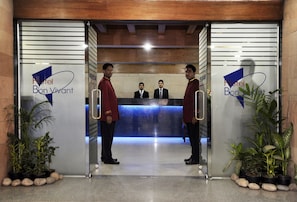 A hotel reception area with a modern design, featuring a reception desk and two uniformed staff members standing at the entrance. - Hotel Bon Vivant (Dhaka)
