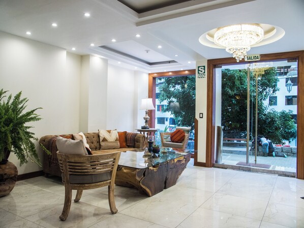 A lobby with a sofa, coffee table, and a wooden chair. There is a chandelier and a sign that reads "SALIDA".