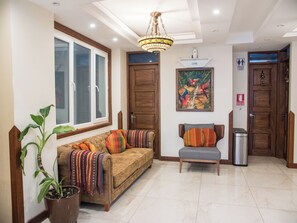 Uma sala de estar com um sofá, um banco, uma planta em vaso e um quadro na parede.