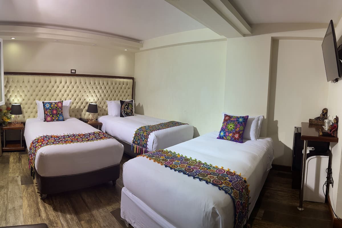 Une chambre d’hôtel avec deux lits, une tête de lit capitonnée, des lampes de chevet et une petite table agrémentée d’objets décoratifs.