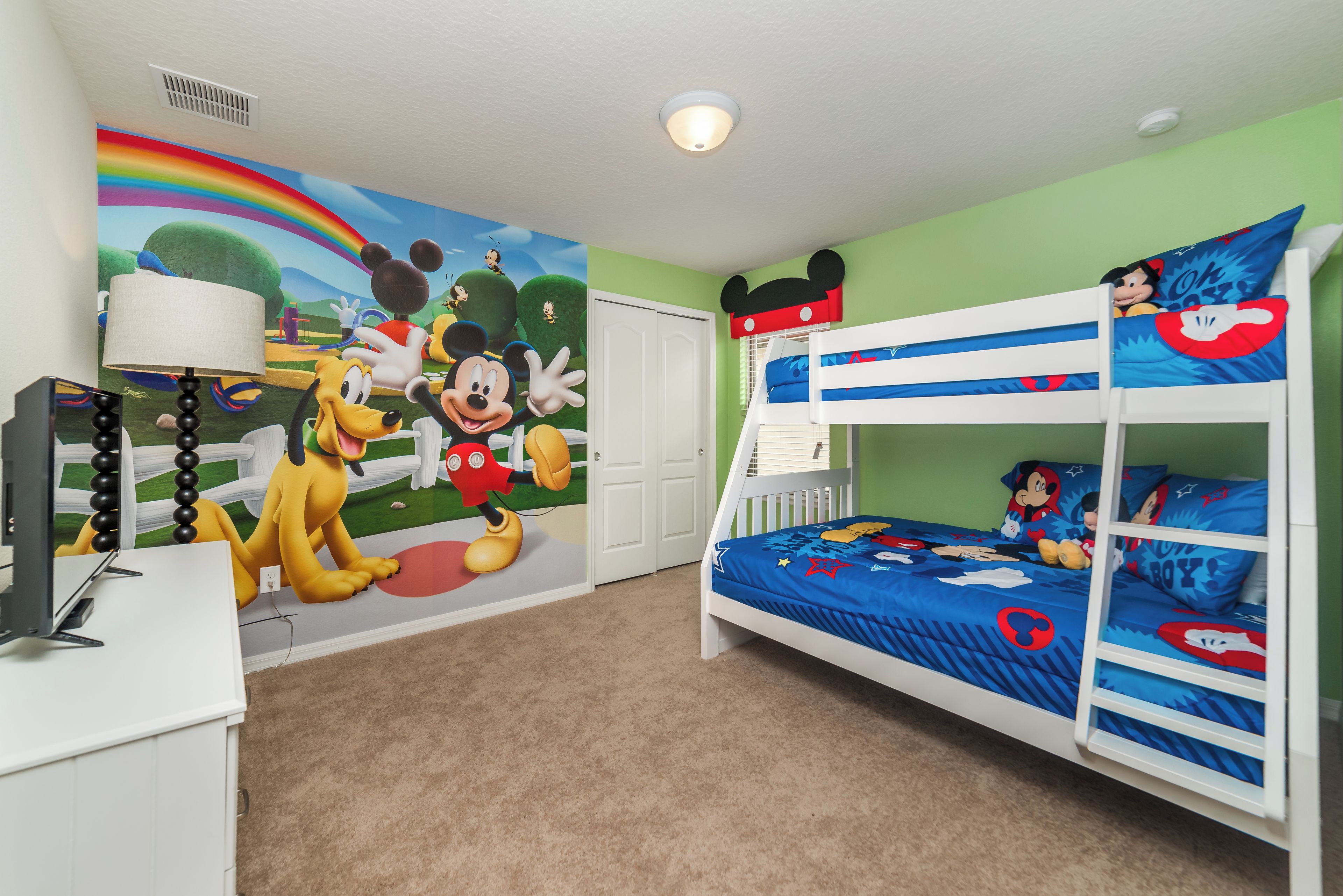 A child's room with a bunk bed, a mural of Disney characters, and a desk with a lamp.