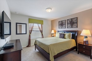A bedroom with a bed, bedside tables, a desk, a TV, and artwork on the walls. - Windsor at Westside Resort Homes (Kissimmee)