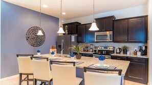A modern kitchen with dark cabinets, stainless steel appliances, and a central island with chairs. - Windsor at Westside Resort Homes (Kissimmee)