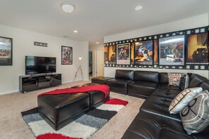 A living room with a TV, black leather sofas, a red throw blanket, and movie posters on the wall. - Windsor at Westside Resort Homes (Kissimmee)