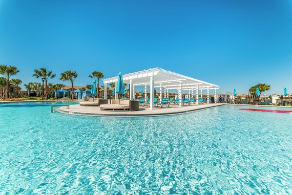 A clear blue pool with a white pergola and lounge chairs, surrounded by palm trees and umbrellas. - Windsor at Westside Resort Homes (Kissimmee)