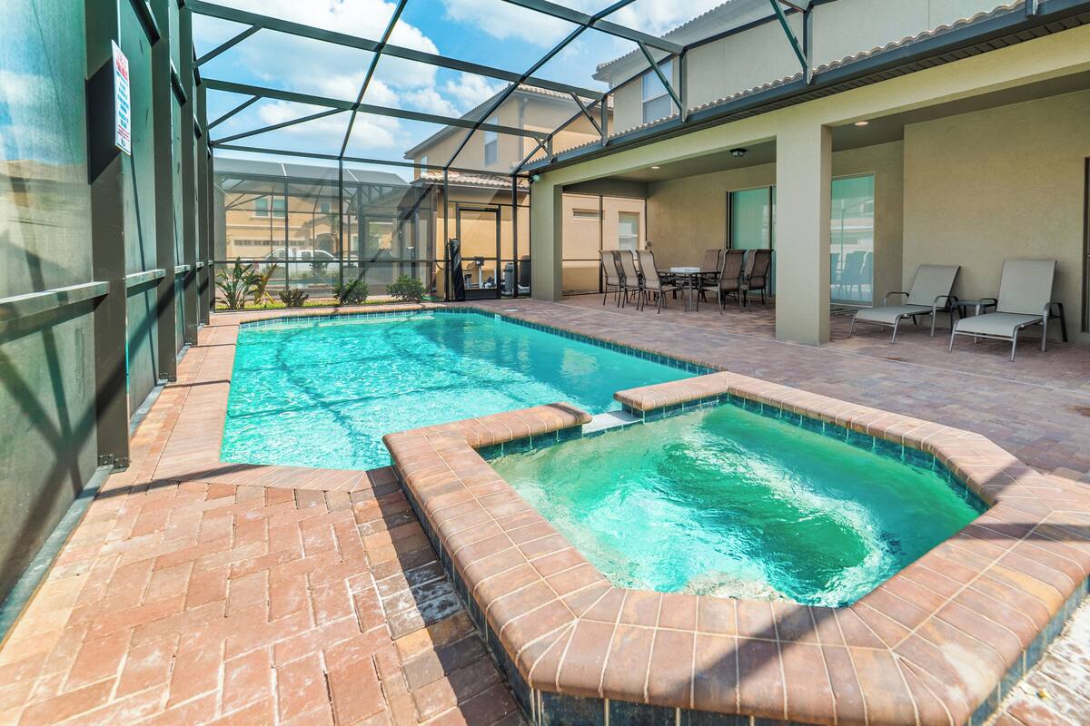 A swimming pool with a glass enclosure, lounge chairs, and a patio area.
