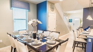 A dining area with a long table set for six, a vase with flowers, and a staircase leading to another room. - Windsor at Westside Resort Homes (Kissimmee)