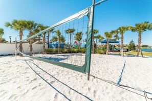 A beach volleyball net set up on a sandy area with palm trees and a clear sky. - Windsor at Westside Resort Homes (Kissimmee)