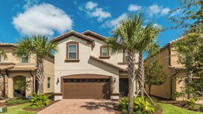 A two-story house with a brown garage, a stone entrance, and a well-maintained lawn with palm trees. - Windsor at Westside Resort Homes (Kissimmee)