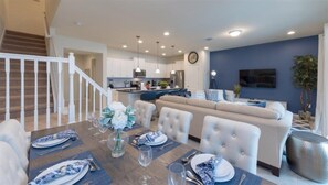 A dining area with a wooden table set for four, a sofa, and a staircase leading to an upper level. - Windsor at Westside Resort Homes (Kissimmee)
