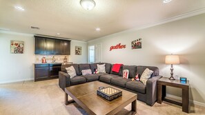 A living room with a sectional sofa, a coffee table, a lamp, and a kitchen in the background. - Windsor at Westside Resort Homes (Kissimmee)