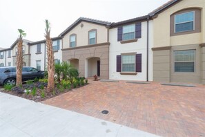A residential building with a paved driveway, palm trees, and a parked car. - Windsor at Westside Resort Homes (Kissimmee)