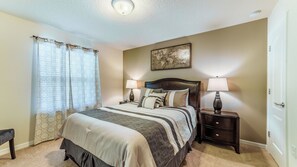 A bedroom with a bed, two bedside tables with lamps, a window with curtains, and a wall-mounted painting. - Windsor at Westside Resort Homes (Kissimmee)