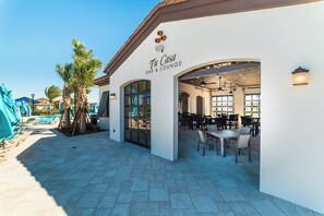 A bar and lounge area with outdoor seating, palm trees, and a clear sky. - Windsor at Westside Resort Homes (Kissimmee)
