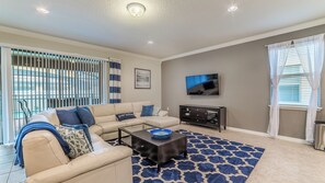 A living room with a sofa, coffee table, TV, and a patterned rug. - Windsor at Westside Resort Homes (Kissimmee)