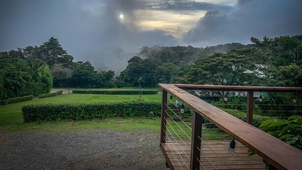 A wooden deck with a metal railing overlooking a park with neatly trimmed hedges and trees. - Casa Campo Verde (Monteverde)