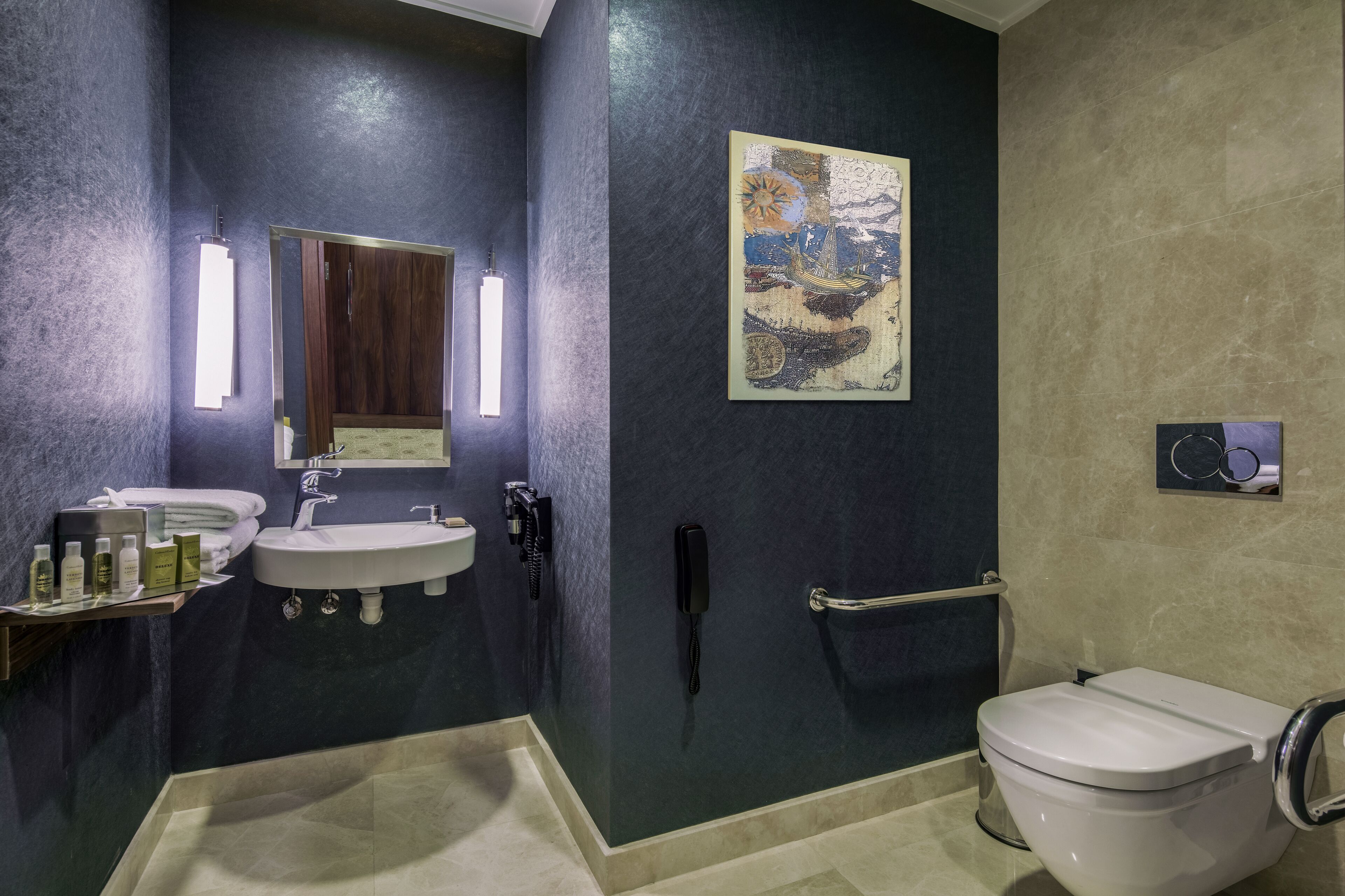 A modern bathroom with a dark blue wall, a white sink, a mirror, a telephone, and a toilet.