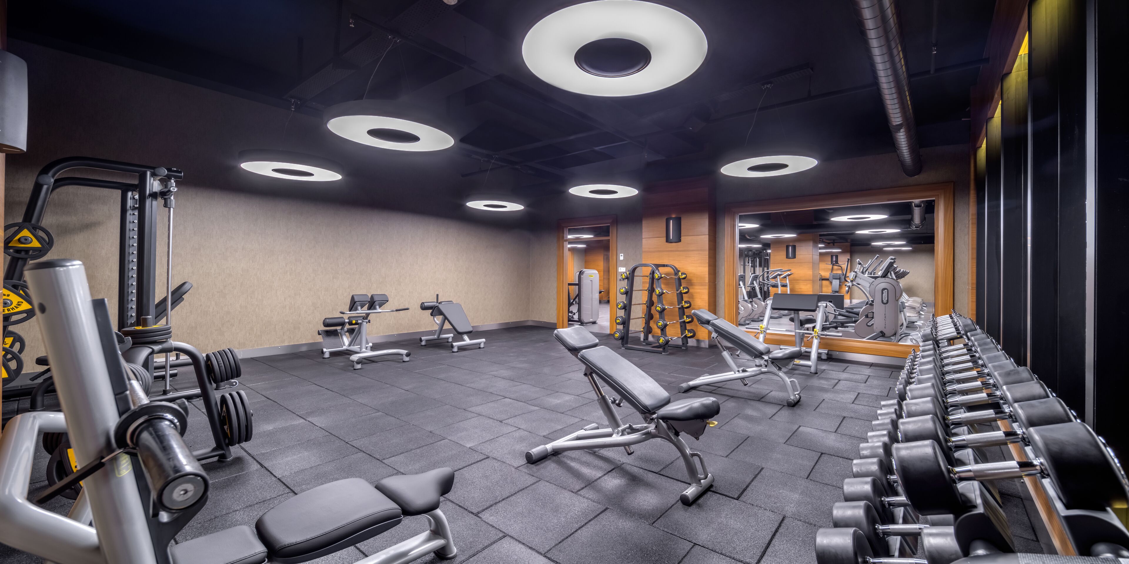 Een sportschool met diverse fitnessapparaten, waaronder banken, gewichten en krachtapparaten.